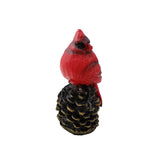Red cardinal figurine on a pine cone against a white background