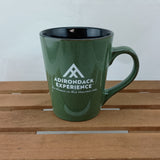 Green mug with Adirondack Experience logo on a wooden surface