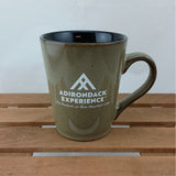 Tan mug with 'Adirondack Experience' logo on a wooden surface