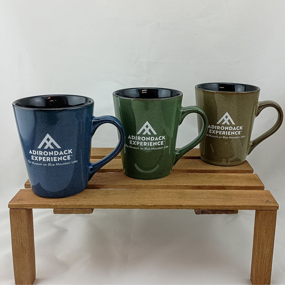 Three mugs with 'Adirondack Experience' logo on a wooden stand against a white background
