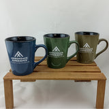 Three mugs with 'Adirondack Experience' logo on a wooden stand against a white background