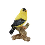 Yellow bird figurine with black wings perched on a branch against a white background