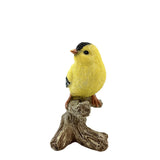 Yellow bird figurine with black wings perched on a branch against a white background