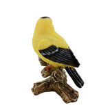 Yellow bird figurine with black wings perched on a branch against a white background